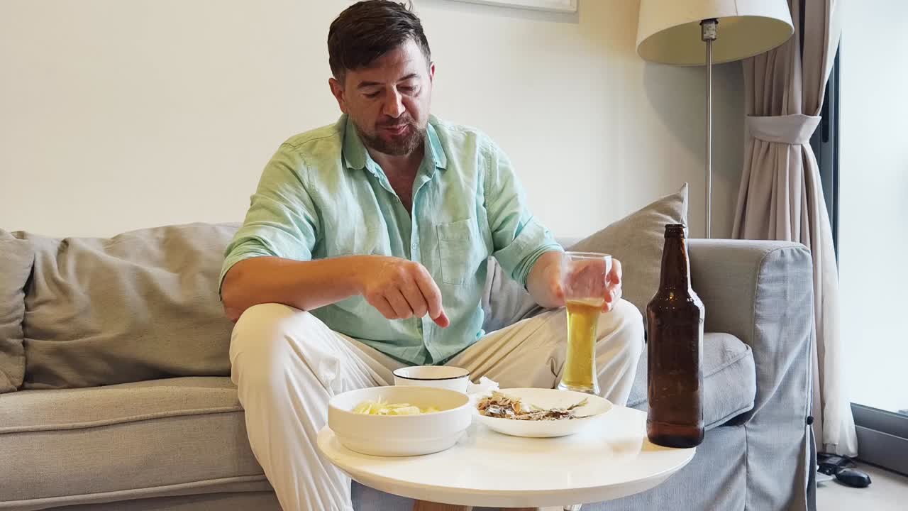 Man eating snacks and drinking beer on sofa