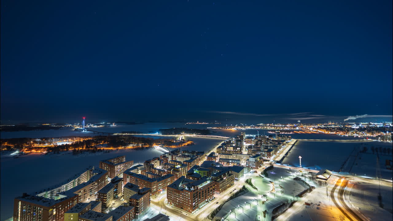 Flygande timelapse av det upplysta Kalasatama-distriktet en vinternatt i Helsingfors