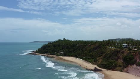 Rising-aerial-drone-shot-of-the-beautiful-tropical-Giz-beach-with-small-waves,-golden-sand,-surrounded-by-cliffs-and-exotic-jungle-in-Tibau-do-Sul-near-Pipa,-Brazil-in-Rio-Grande-do-Norte