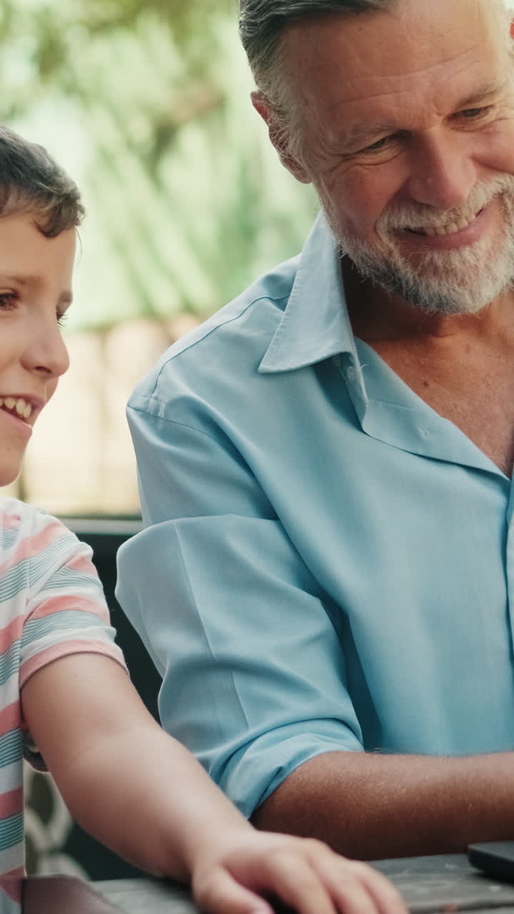 Grandfather and Grandson Smiling While Using Laptop Outdoors