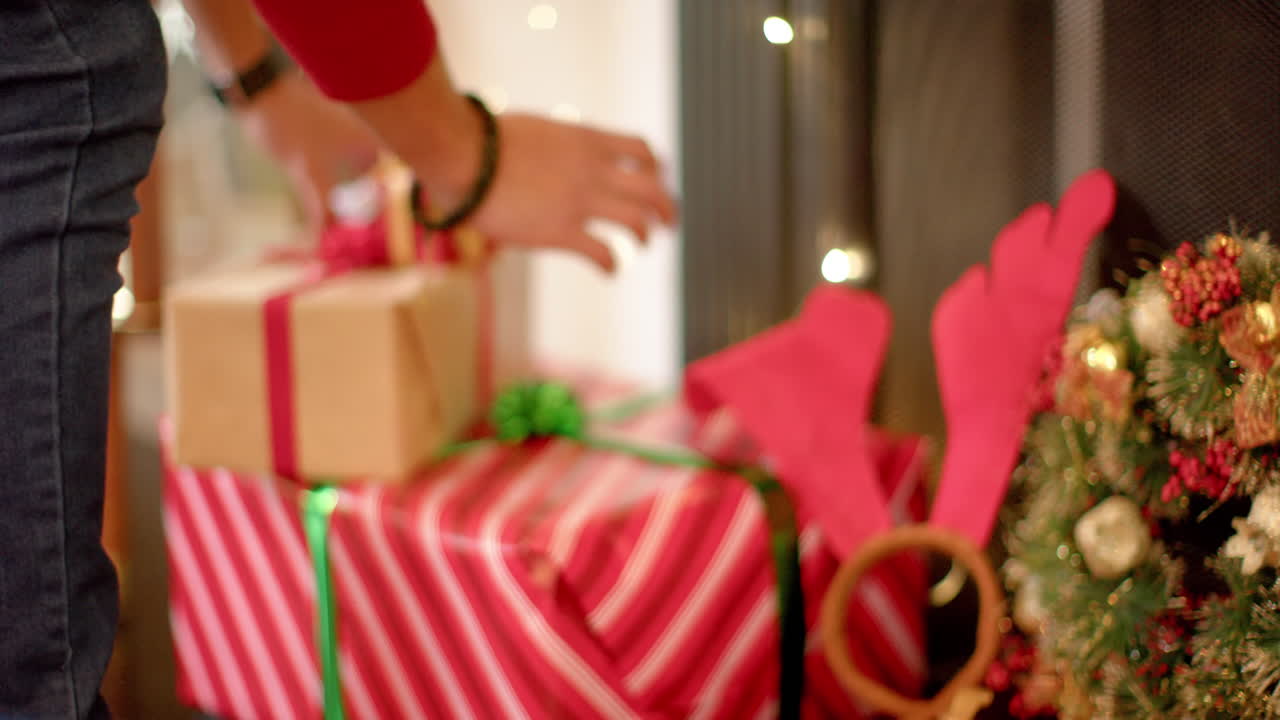hombre biracial poniendo regalo de navidad bajo el árbol de navidad, cámara lenta