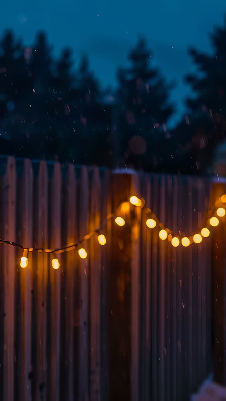 Vertical video: Camera capturing wooden fence with glowing string lights at dusk, showing calm mood