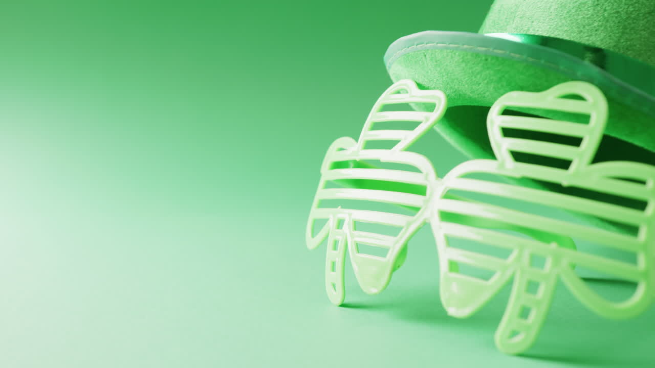 Video of st patrick's shamrock leaf glasses and hat with copy space on green to white background