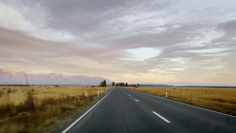 Stunning-road-trip-along-New-Zealand's-countryside-highways-with-mountains-in-background-at-sunrise