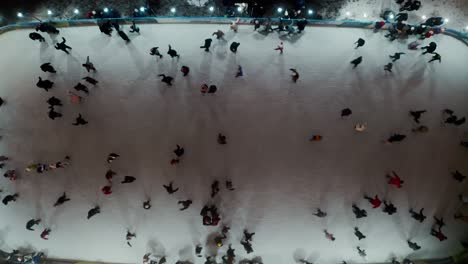 aerial drone view of people skating on an outdoor skating rink in winter at night in city, with dark nighttime lighting.