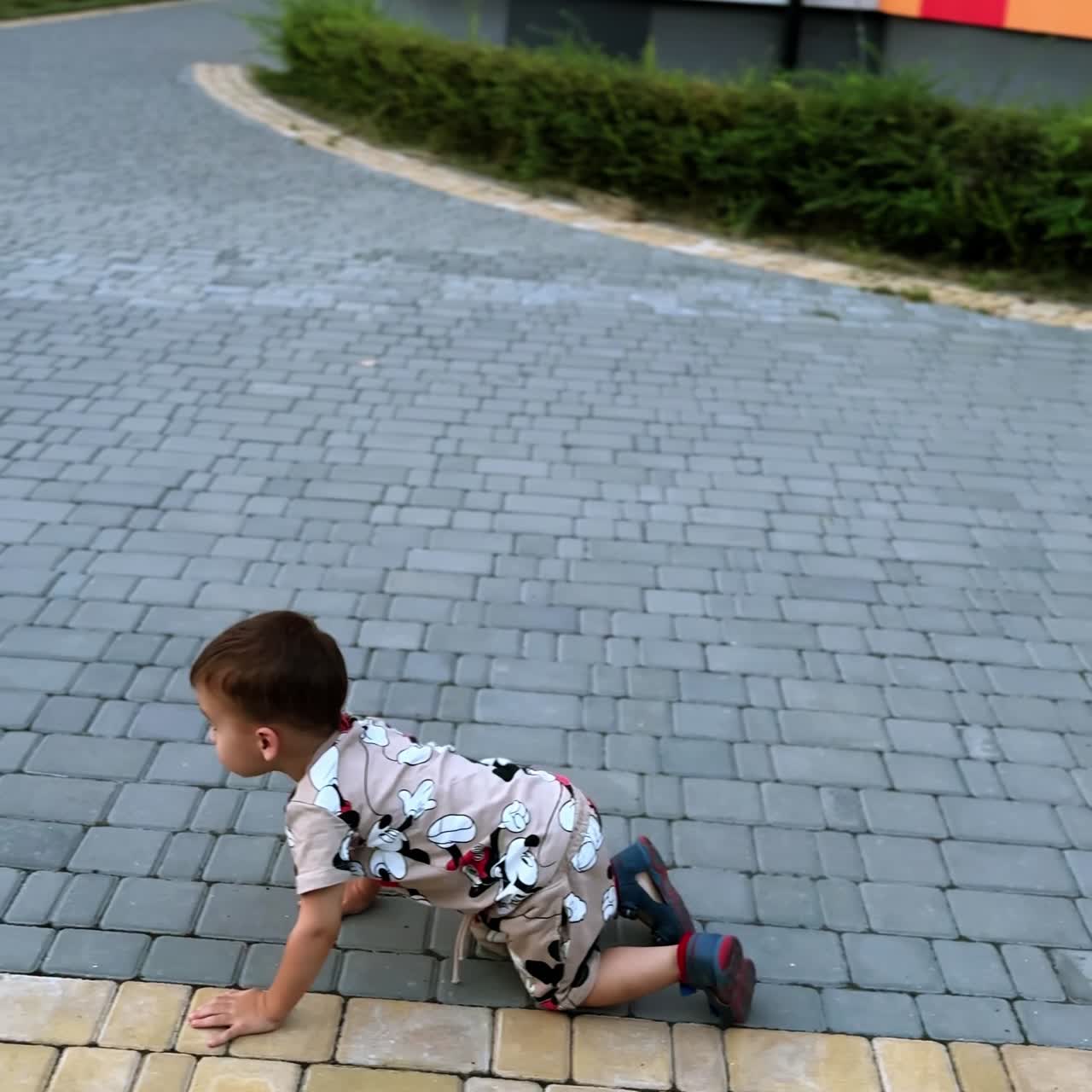 Little Caucasian baby boy playing outside. Kid having fun crawling by the paved ground. Vertical screen