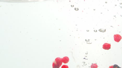 Mixture of different fresh berries dropped into water, isolated on white