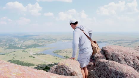 una toma estática amplia de un excursionista masculino con una bolsa de cámara explorando y mirando a través del idílico valle en mount scott, oklahoma