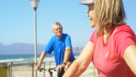 Front-view-of-active-senior-Caucasian-couple-interacting-with-each-other-on-a-promenade-at-beach-4k