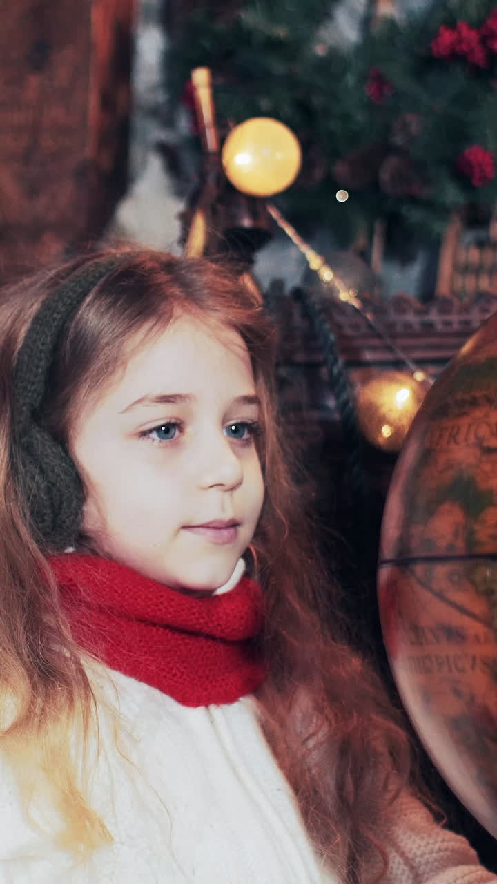 Santa Claus and a beautiful girl are viewing countries on a globe that is spinning. Santa's Christmas Residence. Vertical video