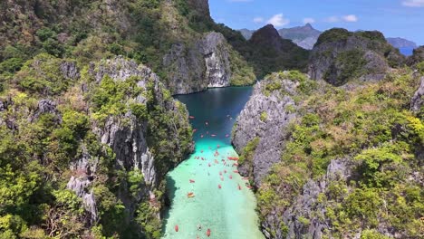 aerial view of big lagoon in miniloc, philippines, with clear turquoise waters, limestone cliffs, lush greenery, and numerous kayakers exploring the tropical paradise under a bright, sunny sky