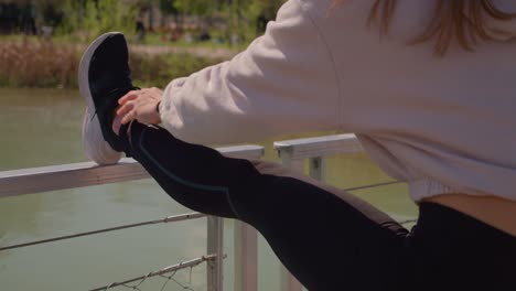 Slim-female-stretching-near-small-water-pond-wearing-black-yoga-pats,-close-up-view