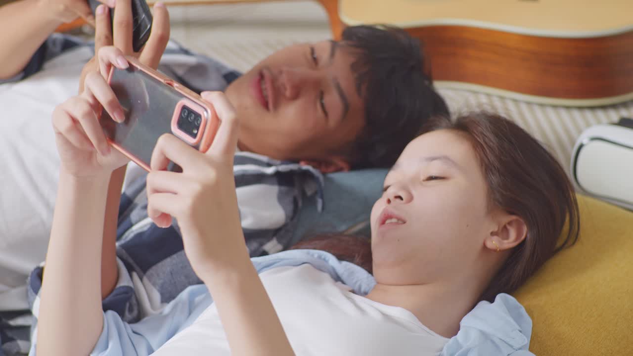 아시아 십대 커플이 집에서 바닥에 카에 누워있는 동안 스마트폰에서 함께 게임을 즐기고 있습니다.