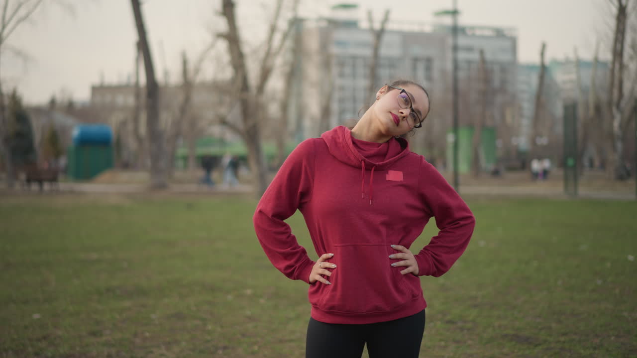 Athlete Standing Calmly During Morning Warmup, Female Sports Performer Poised And Ready On Grassy Field Surface, Confident Female Track Athlete Stands With Hands On Hips Before Sprint Start