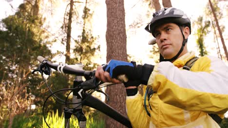 ciclista de montaña masculino llevando una bicicleta en el bosque