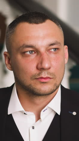 middle aged gentleman with three-day stubble in festive black costume with vest and white shirt with unbuttoned collar stands on staircase in hall slow motion