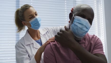 Diverse-female-orthopedic-doctor-examining-male-patient-in-face-masks