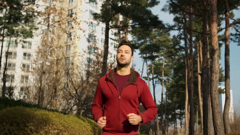attractive man, guy jogging in the park on a background of pine trees and modern apartments - low angle