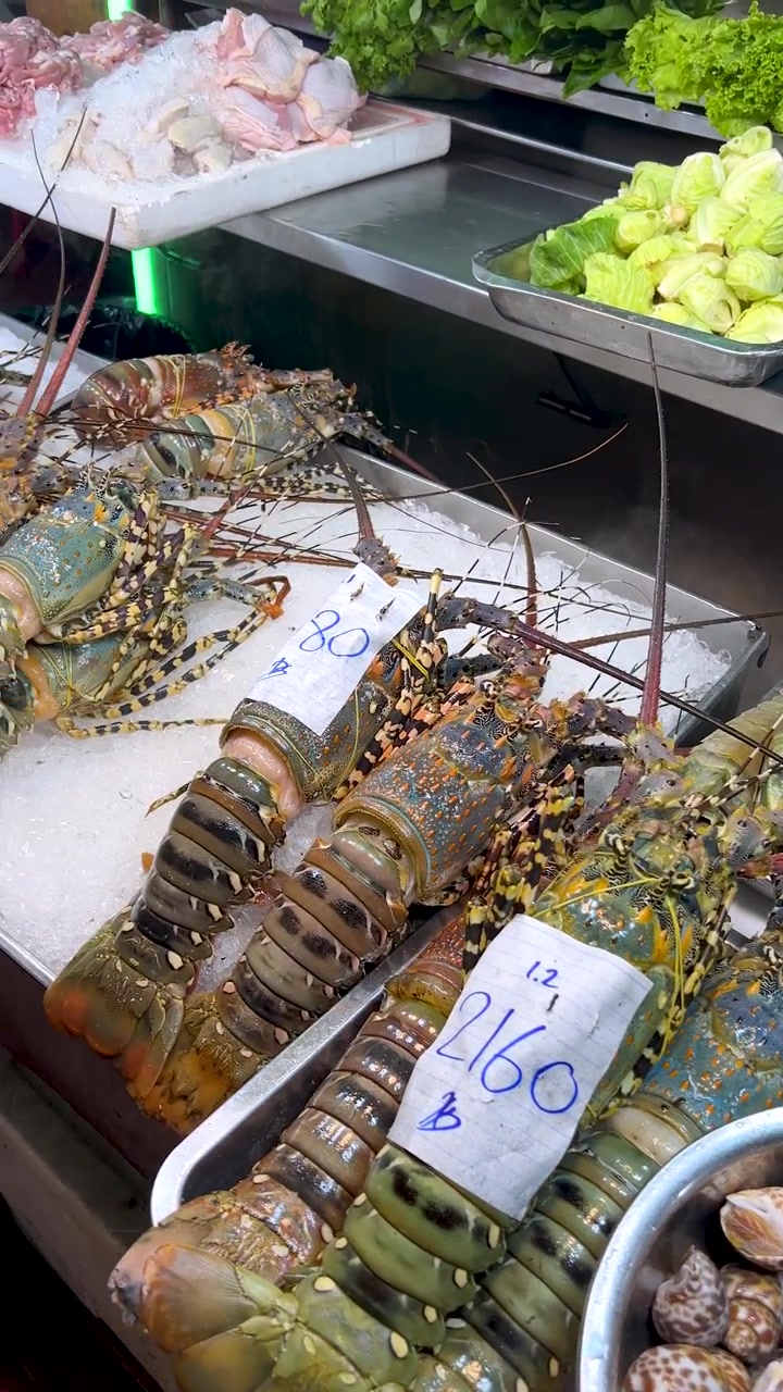 Colorful lobsters and shellfish displayed on ice at night market, camera pans across seafood selection