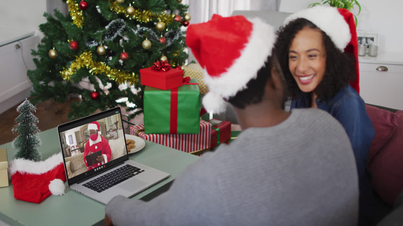 pareja afroamericana con sombreros de santa haciendo una videollamada en una computadora portátil en casa durante la navidad
