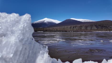 una vista prístina de un río congelado con montañas cubiertas de nieve en el fondo bajo un cielo azul claro en rusia durante el invierno