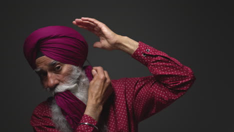 close up low key studio lighting shot de un anciano sikh con barba usando aguja salai cuando se pone el turbante contra un fondo oscuro shot en tiempo real 2