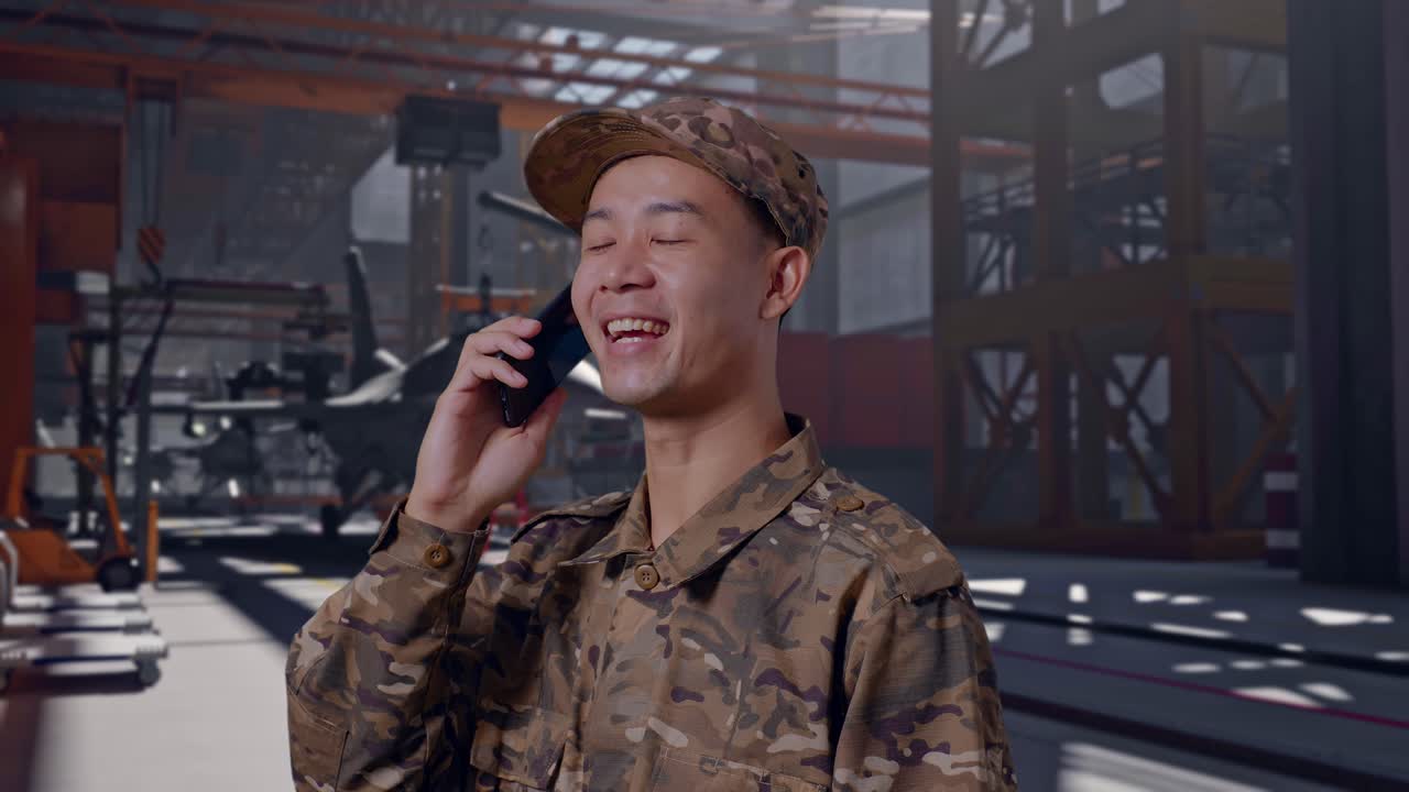 Soldato asiatico che parla al telefono e sorride in un hangar militare
