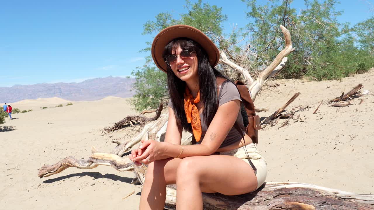 Giovane donna felice seduta su legno secco nel deserto