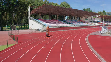 following the person in funny dinosaur costume running along the tack. tirex dinosaur jogging around the stadium.