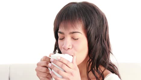 Smiling-woman-sitting-on-sofa-with-hot-beverage