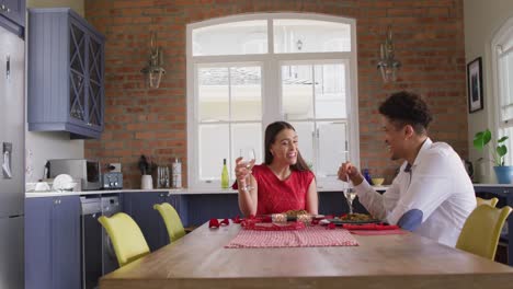 feliz pareja biracial que celebra el día de san valentín comiendo en casa