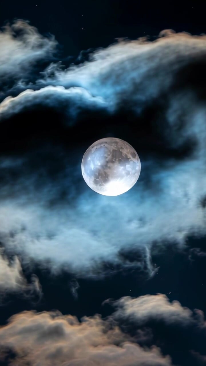 Vídeo vertical: Nuvens flutuantes movendo-se com a brisa pelo céu noturno, revelando e obscurecendo a lua cheia.