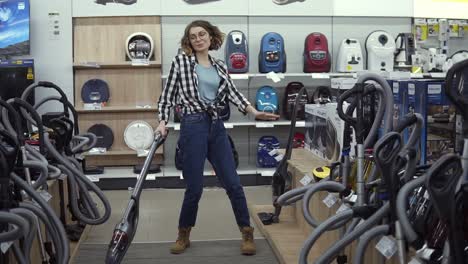 funny caucasian woman in casual standing in home appliance store - dancing, having fun with hand helded vacuum cleaner, funky dances