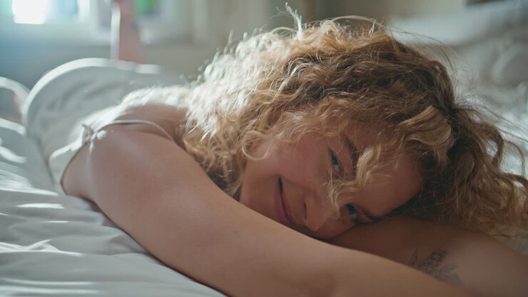 Nahaufnahme: Frau lacht im Bett am Morgen. Verspieltes Mädchen entspannt gemütlich zu Hause.