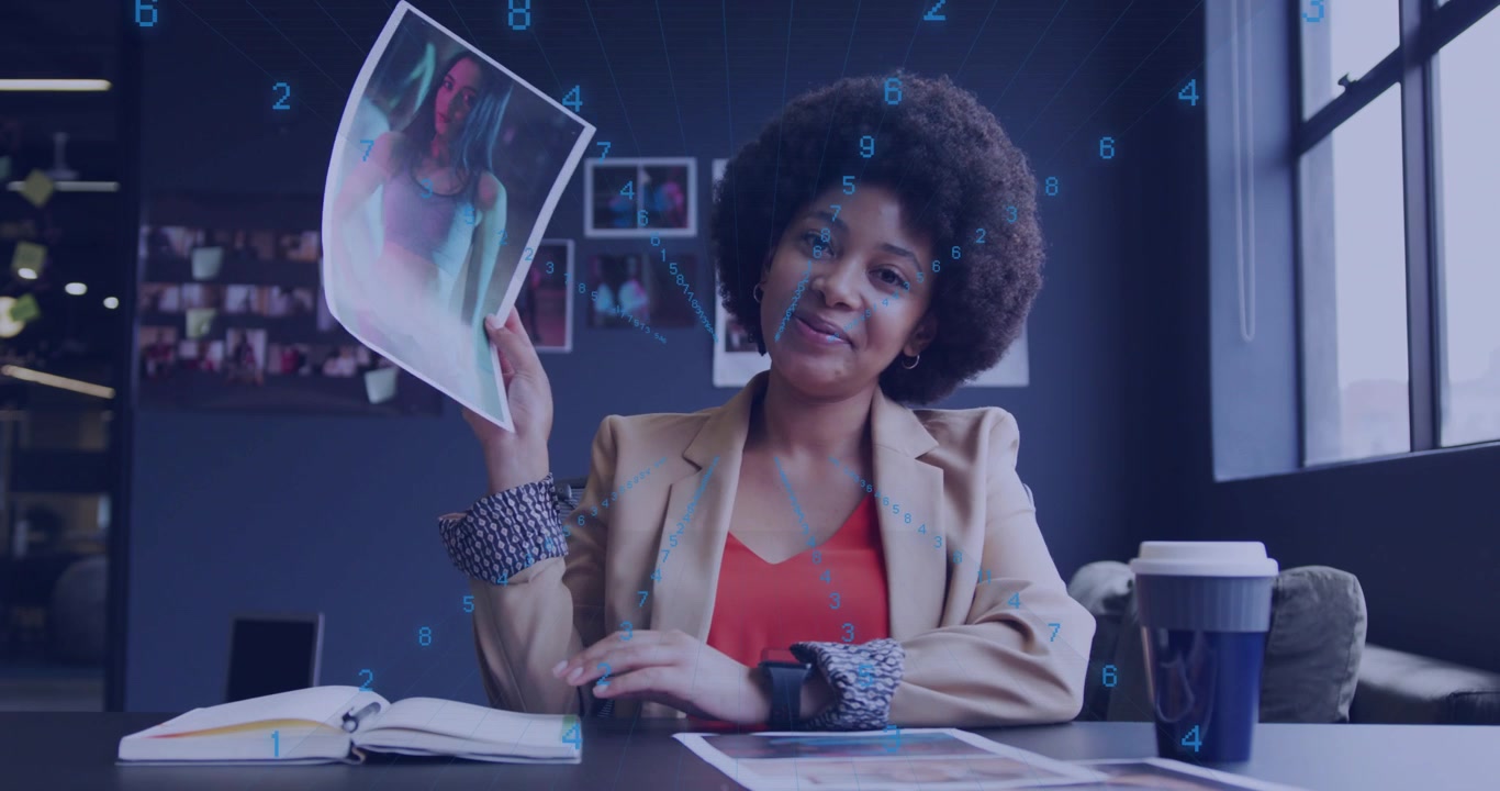 Designer at desk flipping pages, lifting print, pointing at detail for review, blue data drifting