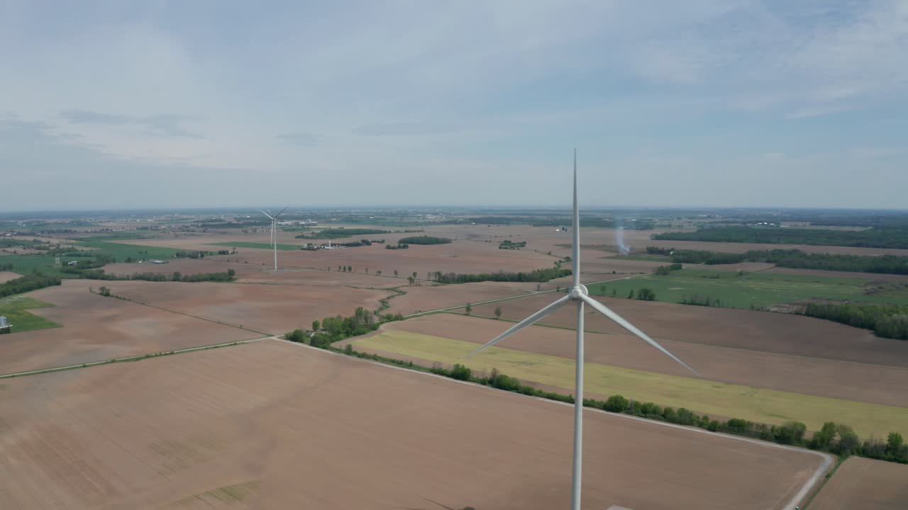 Massive windmills turn in the breeze over farm fields and flat terrain