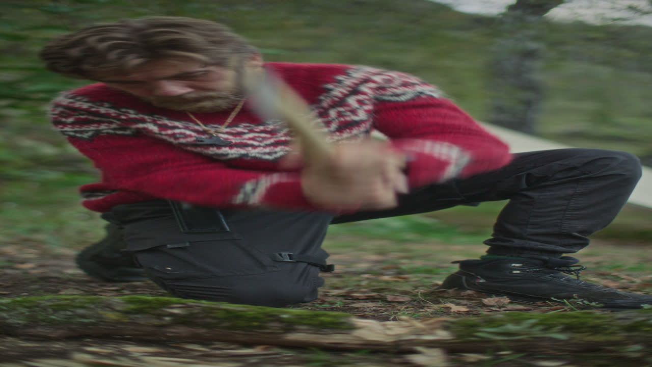 Survivalist Chopping Mossy Log with Axe in Forest Camp