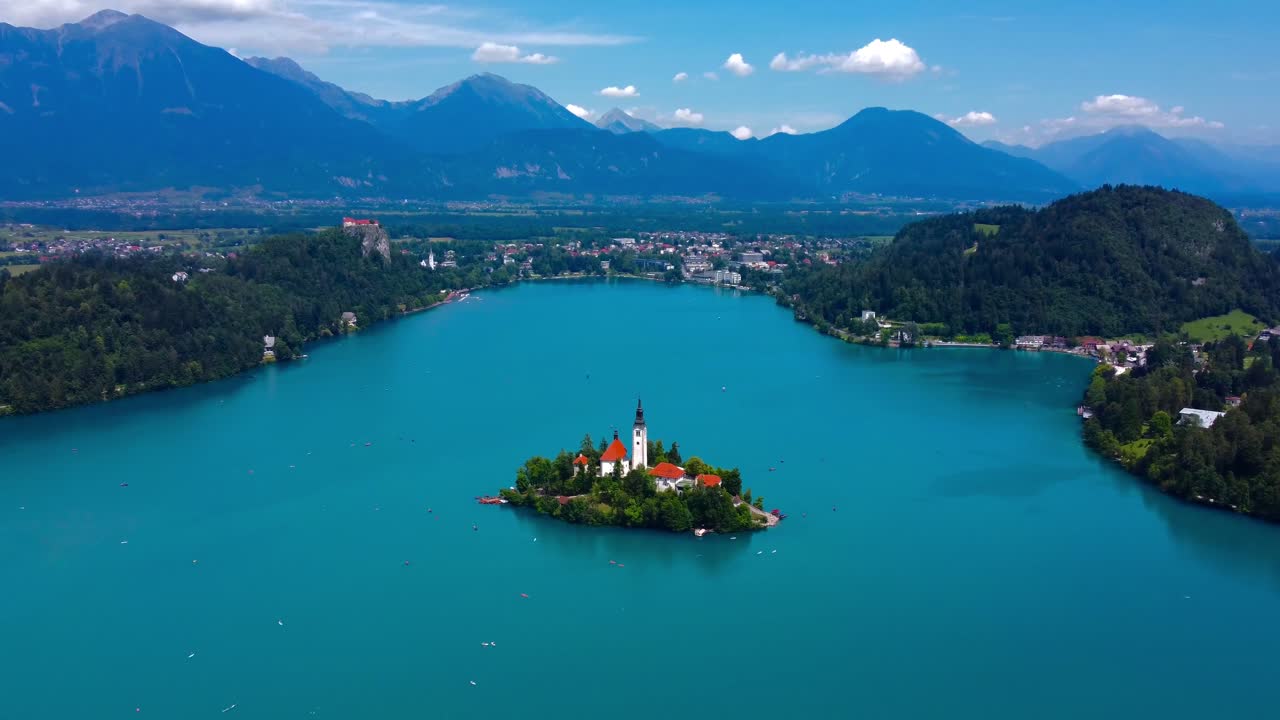 Drone aerial view in 4K of iconic Lake Bled with island - turquoise blue water and green trees on beautiful summer's morning