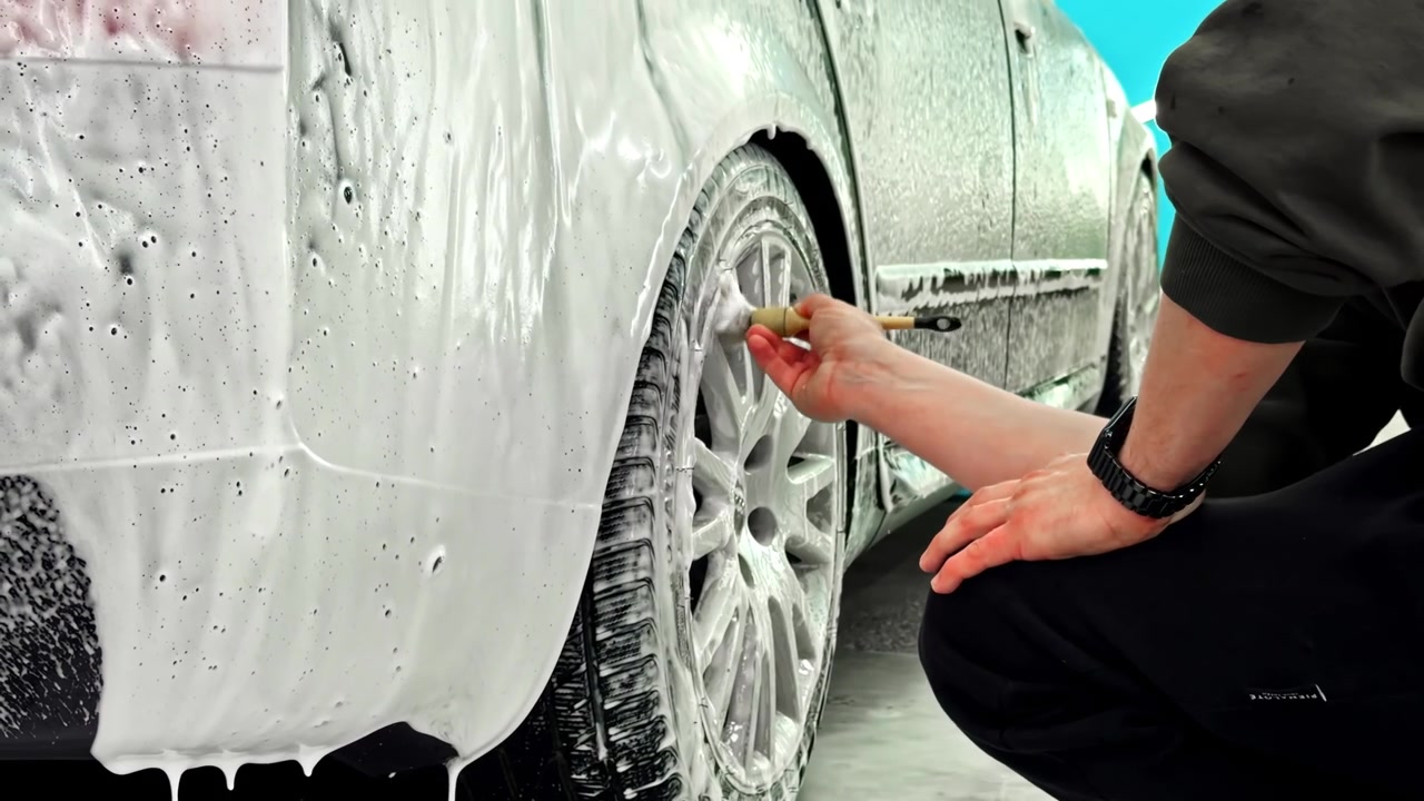 Person Uses Cleaning Brush To Scrub Soap Suds Off Car Wheel During Detailing Process. close-up, side view shot