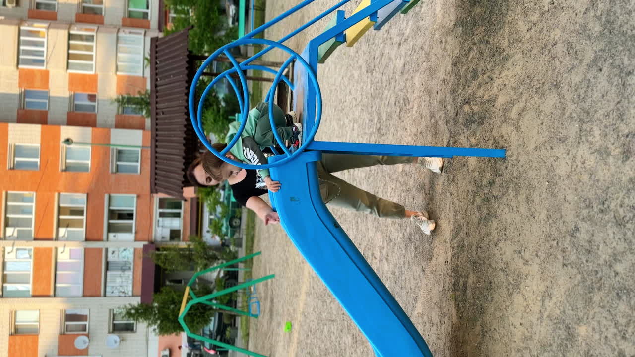 Caring mom holding her child sliding on the playground. Happy baby having good time outdoors. Vertical video.