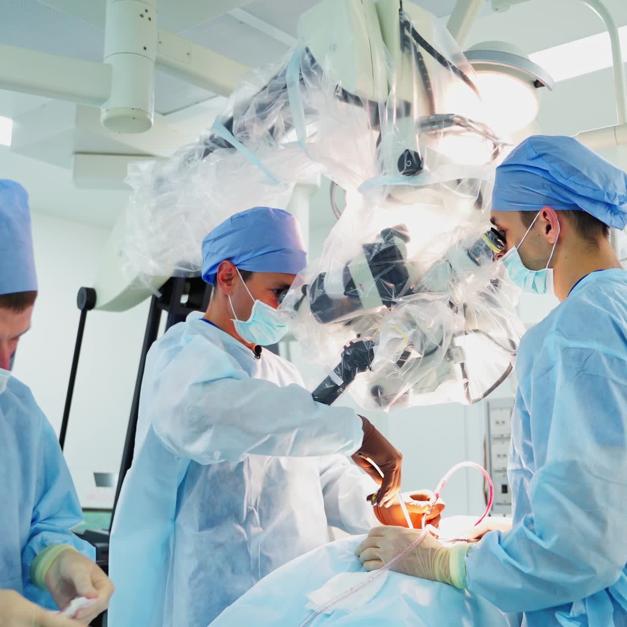 Teamwork of doctors in medical uniform in modern clinic. Group of doctors conduct a microsurgical operation with microscope. Neurosurgery concept.