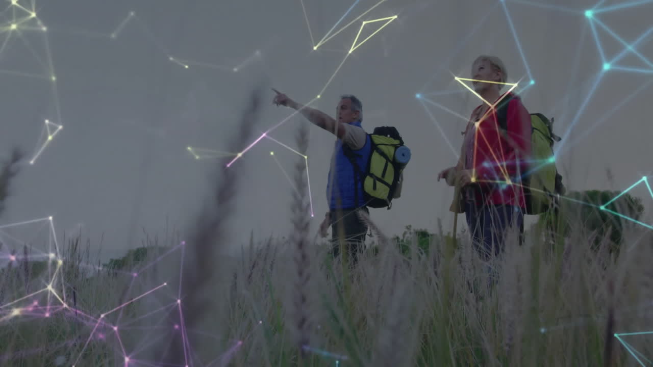 Senior hikers pointing toward horizon in meadow, showing glowing nodes and lines tech overlay