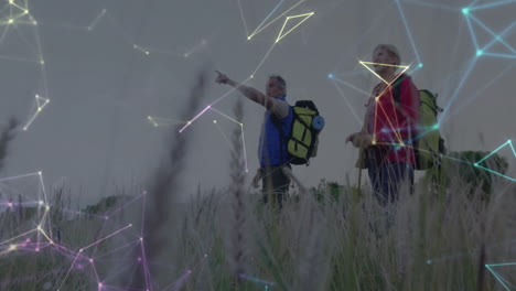 senior hikers pointing toward horizon in meadow, showing glowing nodes and lines tech overlay