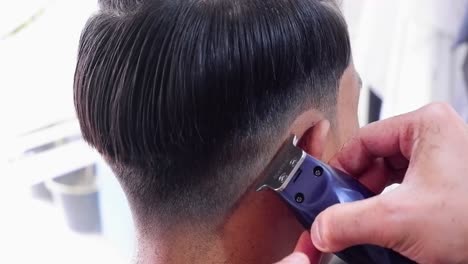 peluquero con cortapelos corta a un hombre en una silla en un salón de barbería usando un cortapelos eléctrico