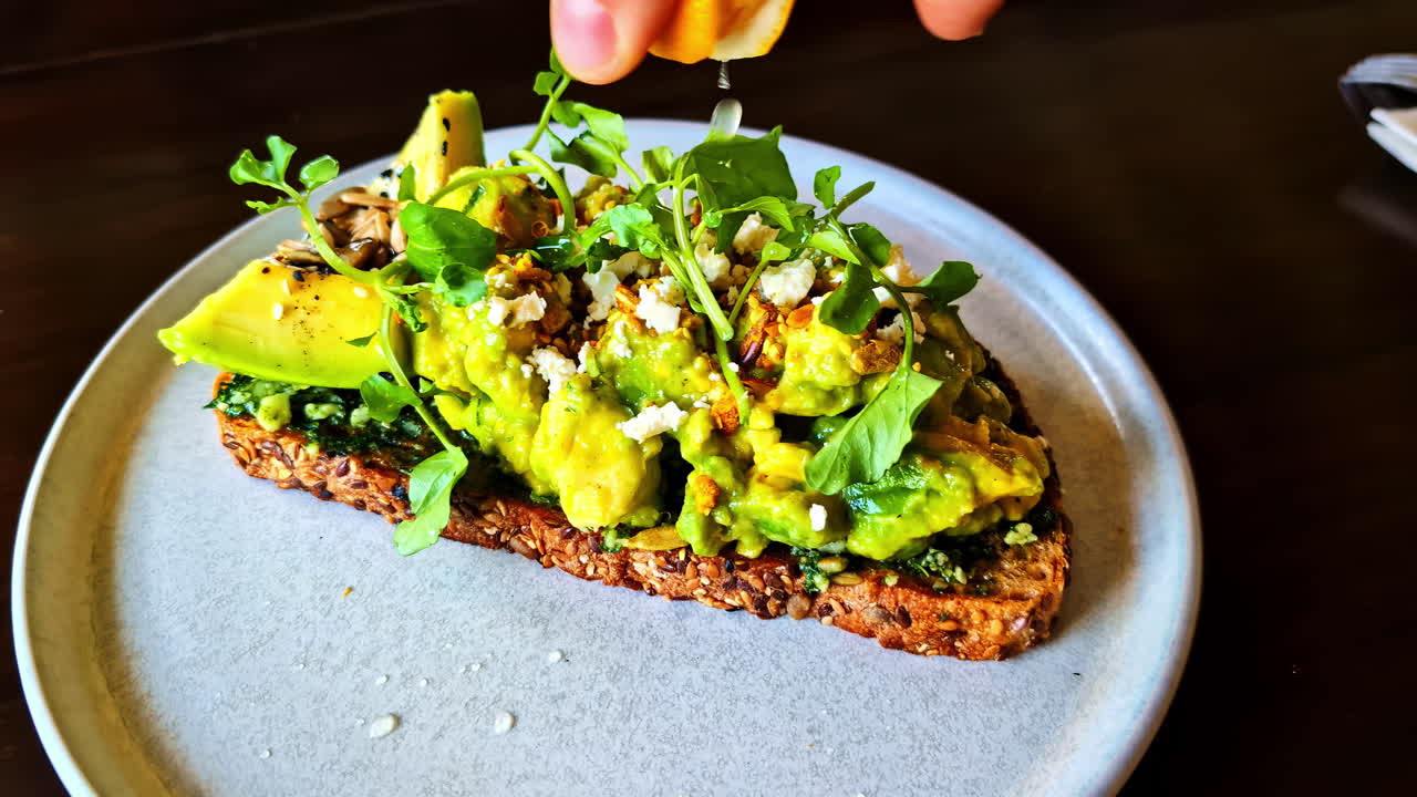 Avocado toast with a sprinkle of greens and cheese, garnished with a squeeze of lemon