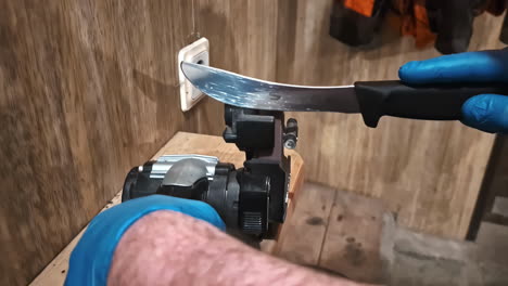 sharpening a large curved knife with a belt grinder, held against the moving abrasive belt.