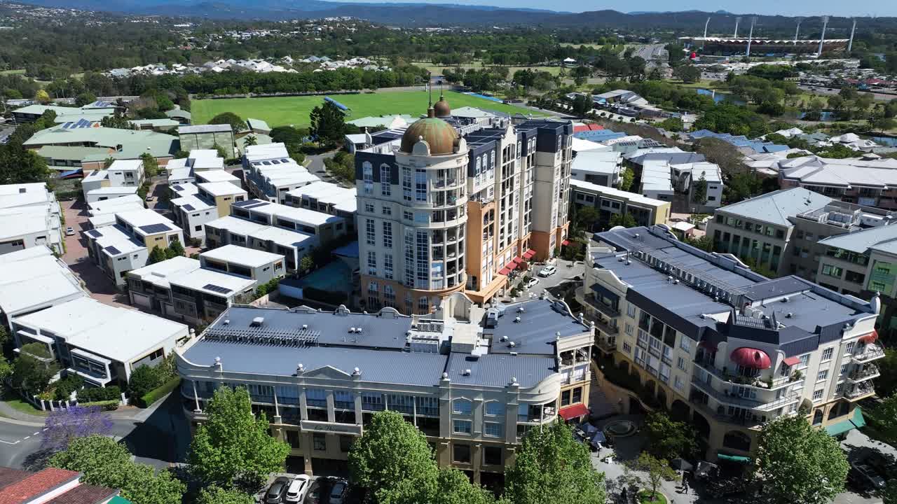 Flying over Emerald Lakes village, enjoy stunning views of the lush greenery and tranquil waters, with the iconic Carrara Stadium visible in the distance. Beautiful scenery from above!
