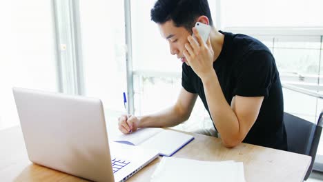 business executive writing on diary while talking on mobile phone