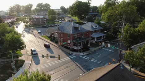 static aerial establishing shot of small town in america, house on corner of intersection at traffic signal light, cars stopped at light, traffic drives on road, drone above rooftop, summer light