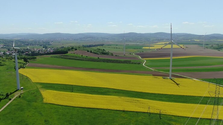 Aerial pan across wind farm turbines and yellow rapeseed fields in countryside